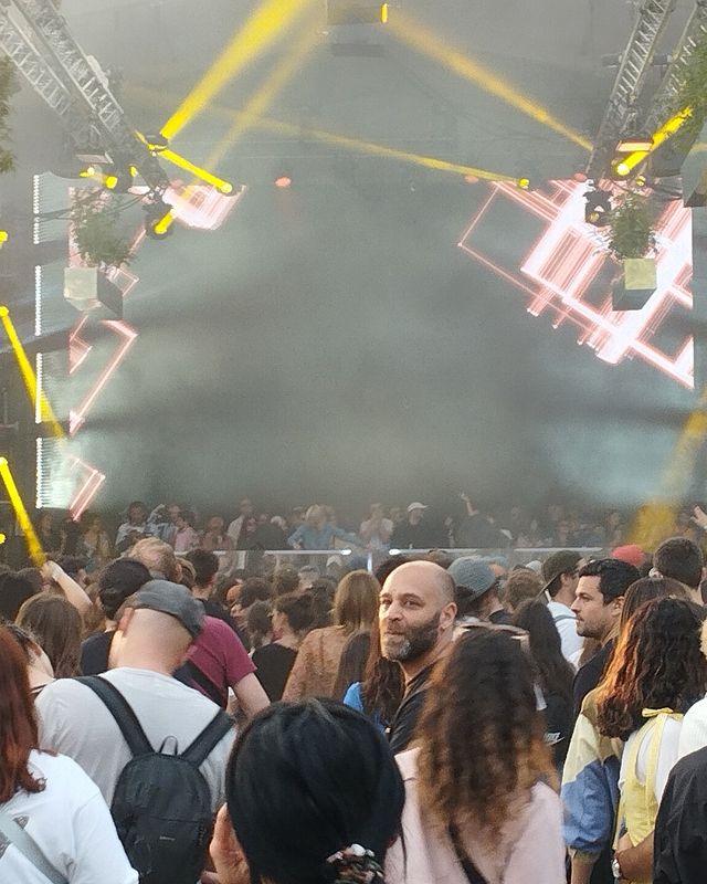 Festival crowd in front of a stage with white beams and a disco ball
