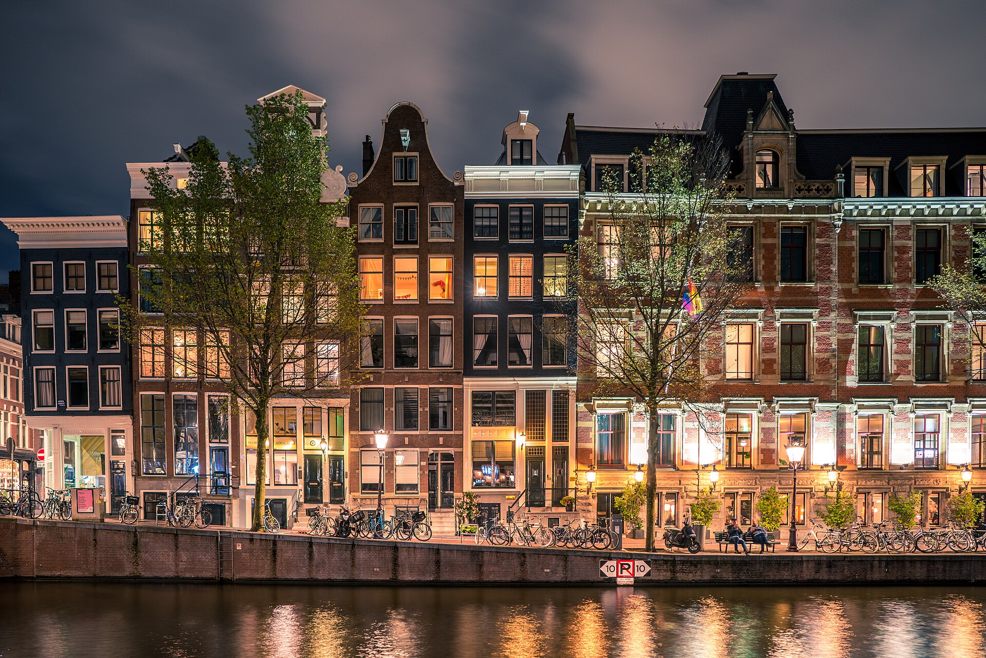 Illuminated canal houses reflected in an Amsterdam canal at blue hour